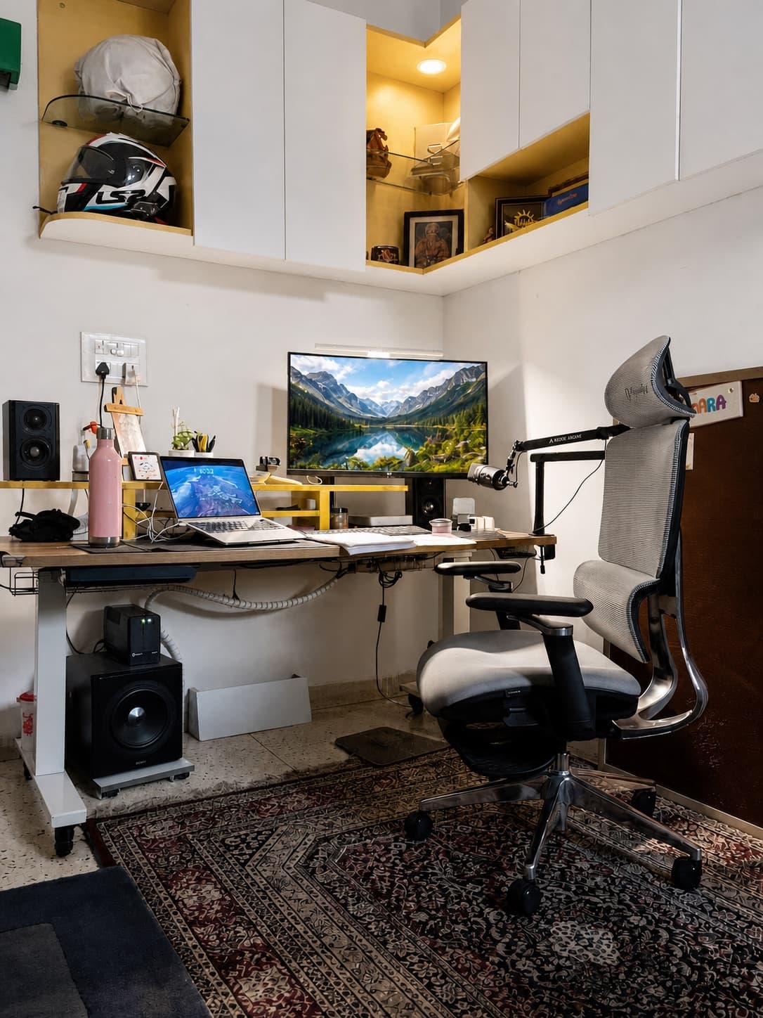 My desk in Delhi NCR — standing desk, dual screens, boom microphone, yellow shelves, and the helmet from the morning ride.